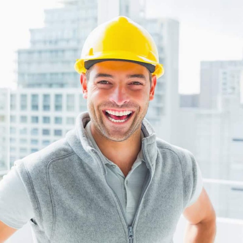 Portrait of cheerful handyman wearing hardhat with buildings in background